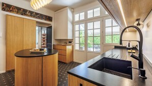 A modern kitchen with a central island, a built-in oven, and a large window providing natural light. - Villa du Val - Welkeys (Aix-en-Provence)