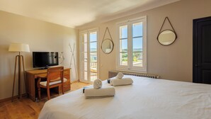 A hotel room with a bed, a desk with a TV, two windows, and a door. - Villa du Val - Welkeys (Aix-en-Provence)