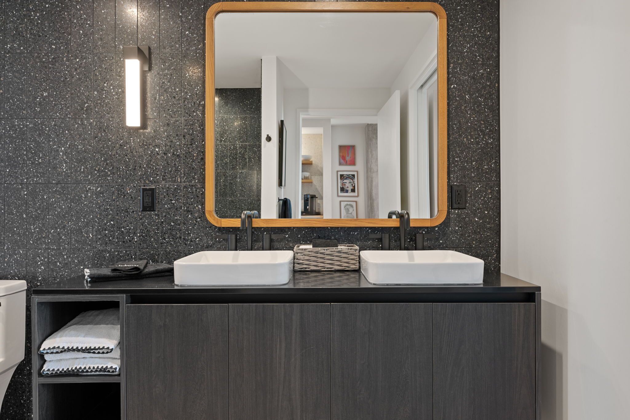 Een moderne badkamer met twee wastafels, een grote spiegel en een donkere, gespikkelde wand.