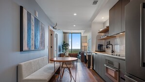 Eine moderne Küche mit Einbauofen, eine Essecke mit rundem Tisch und Stühlen sowie ein großes Fenster mit Blick ins Freie.