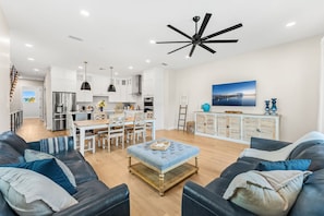 Une cuisine moderne avec des meubles blancs, un coin repas avec une table et des chaises en bois, un canapé en cuir noir et un ventilateur de plafond.