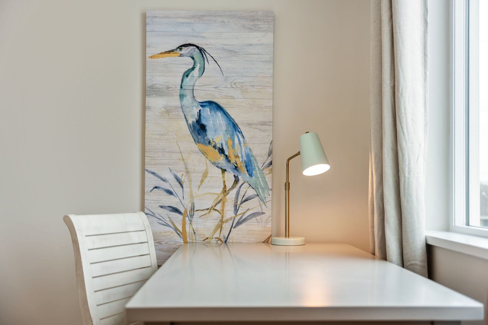 A dining area with a table, a chair, a wall-mounted painting of a bird, and a floor lamp.