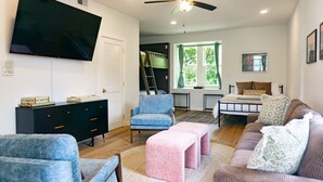 A living room with a flat-screen TV, a ceiling fan, a bunk bed, and a large window with a view of greenery.