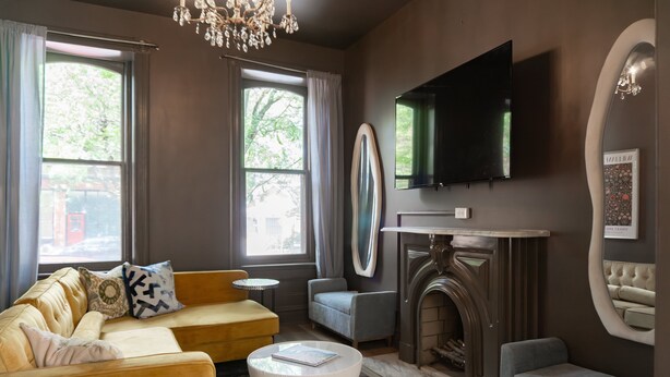 A modern living room with a sofa, armchair, fireplace, and a flat-screen TV mounted on the wall.