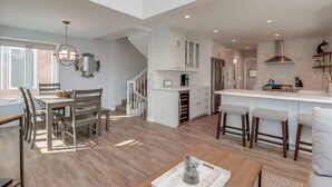 A spacious kitchen with white cabinets, a central island with stools, and a dining area with a wooden table and chairs. - Steps to Bay & Beach | Rooftop Deck, Fire Pit, AC, Garage, Views (San Diego)