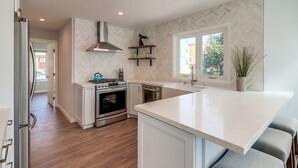 A modern kitchen with white cabinetry, a stainless steel range hood, and a built-in oven. There is a window providing natural light and a view of the outside. - Steps to Bay & Beach | Rooftop Deck, Fire Pit, AC, Garage, Views (San Diego)
