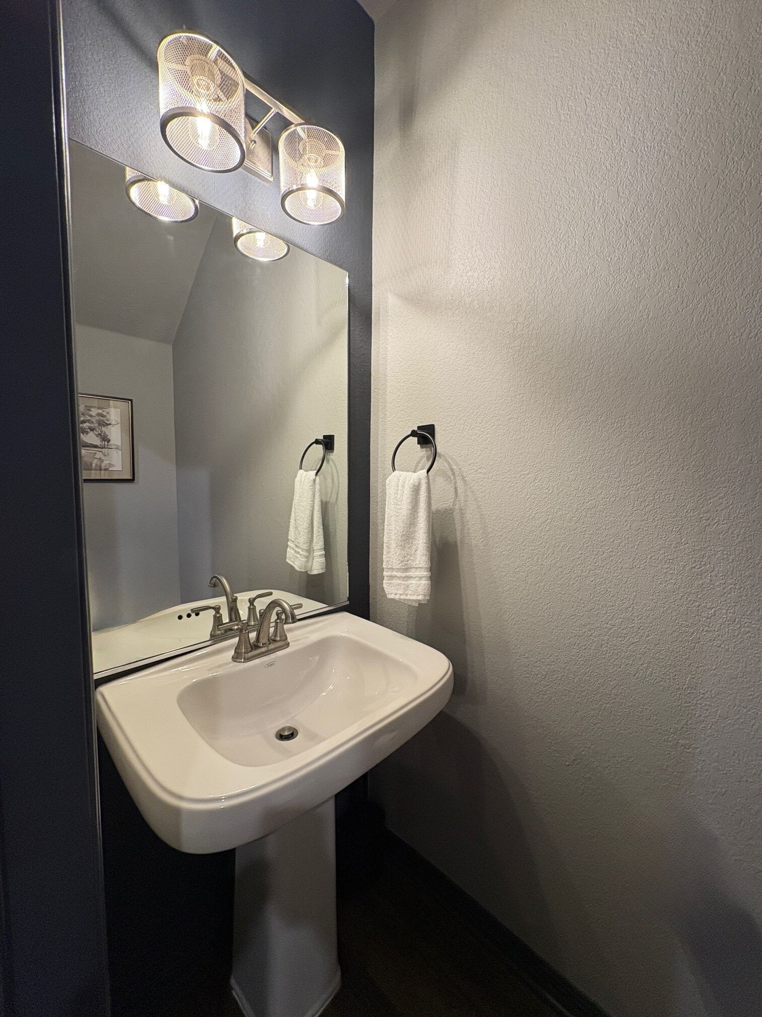 Une salle de bain avec un lavabo blanc, deux porte-serviettes et un miroir agrémenté de trois appliques murales.