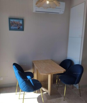 Una habitación pequeña con una mesa de madera y dos sillas azules, un cuadro en la pared y un equipo de aire acondicionado arriba.