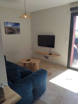 A modern living room with a blue sofa, a small round table, a mounted TV, and a hanging light fixture.