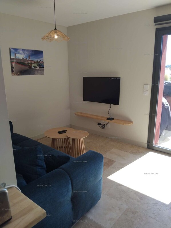 A modern living room with a blue sofa, a small round table, a mounted TV, and a hanging light fixture.