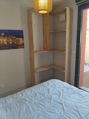 A bedroom with a bed, a hanging light fixture, and a wooden shelving unit.