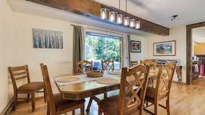 A dining area with a wooden table, chairs, and a view of the outdoors. - Lodge at Deception Pass by Avantstay Trails, Hot Tub, Walk to Cornet Bay (Oak Harbor)