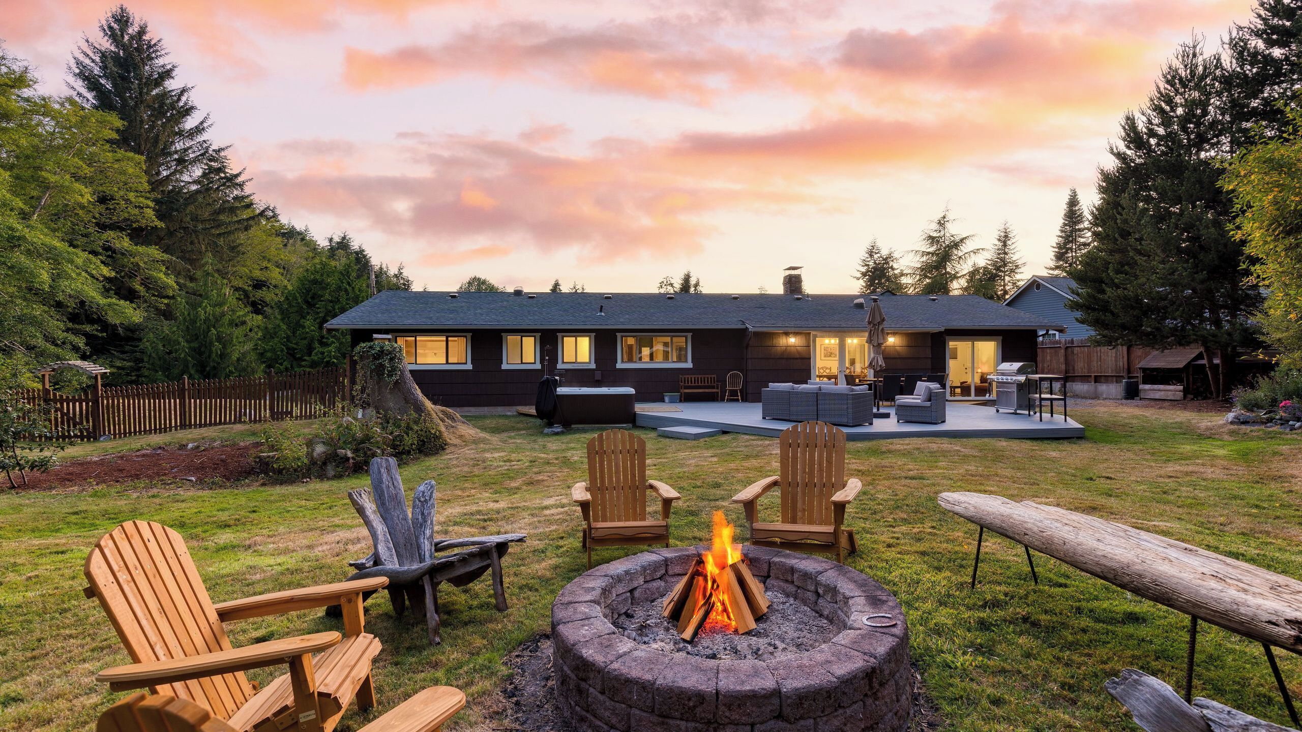 A modern house with a backyard featuring a fire pit, outdoor seating, and a barbecue area.