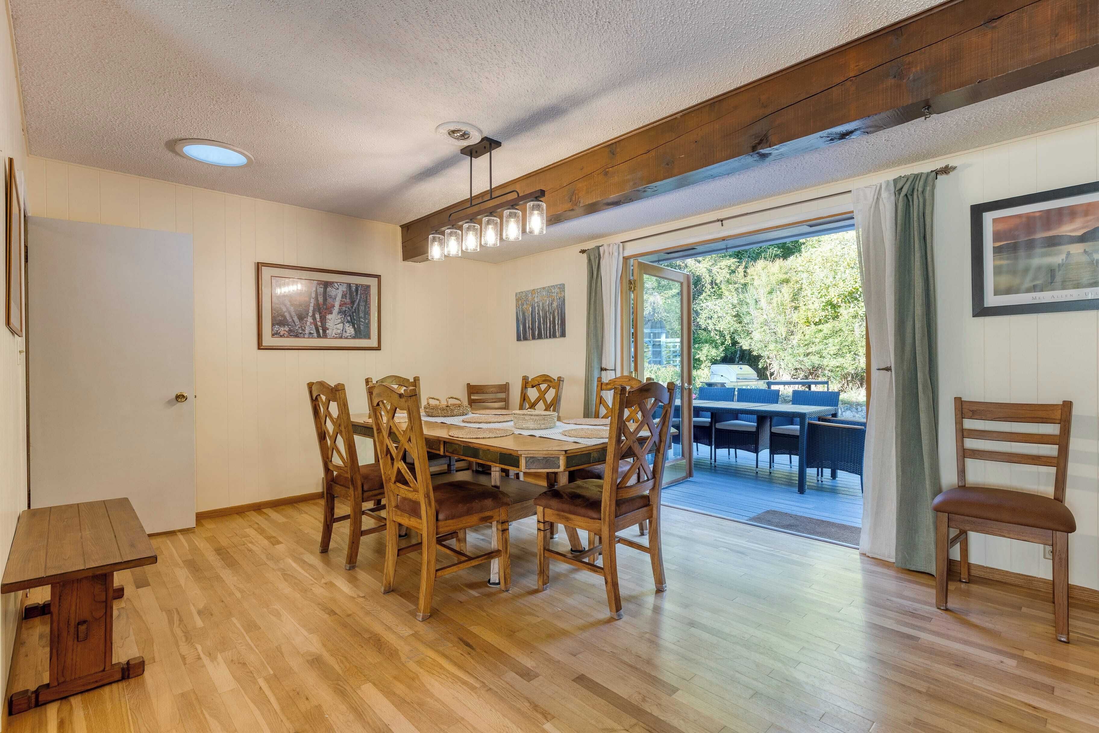 A dining area with a wooden table and chairs, a ceiling light fixture, and a view of the outdoors through a door.