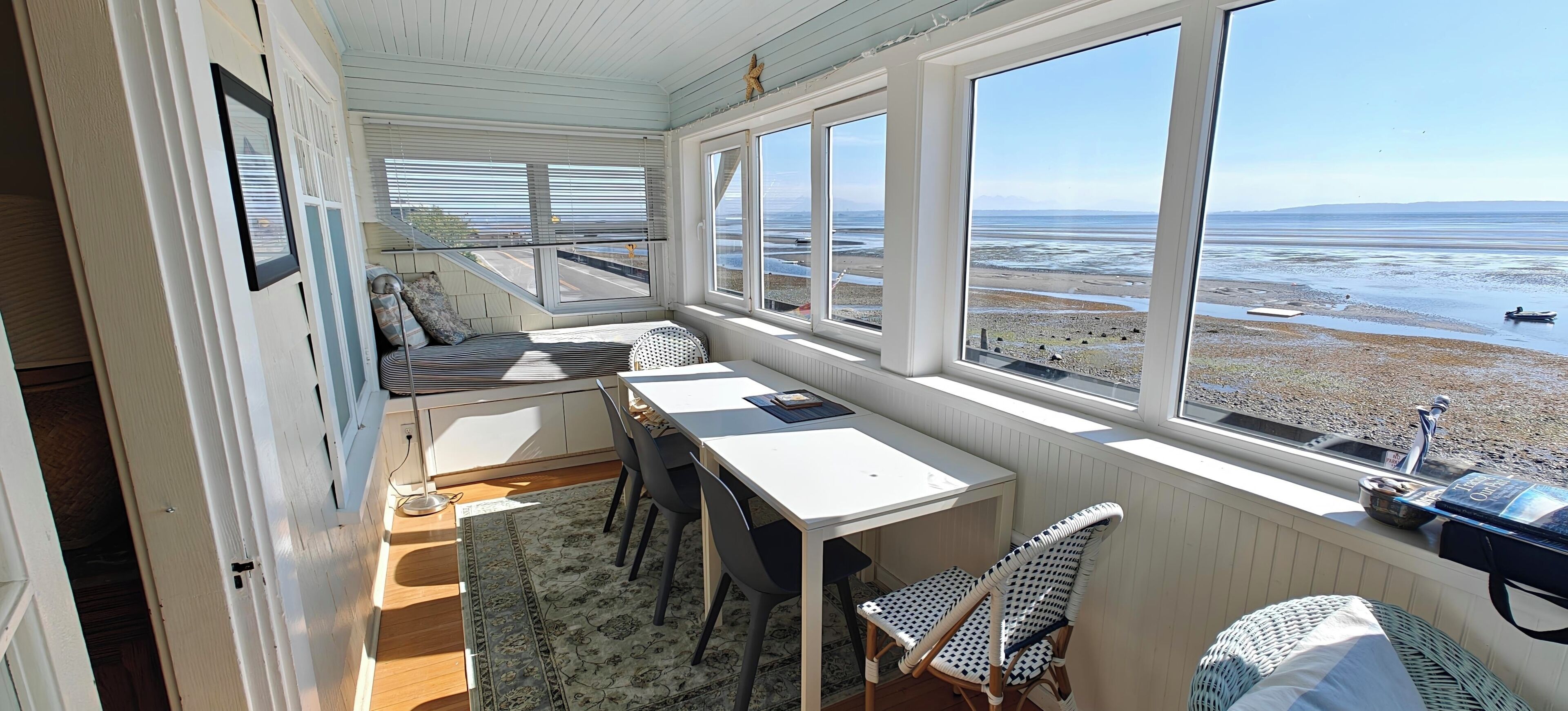 Een kamer met een eettafel, stoelen, een bank en grote ramen met uitzicht op een strand.