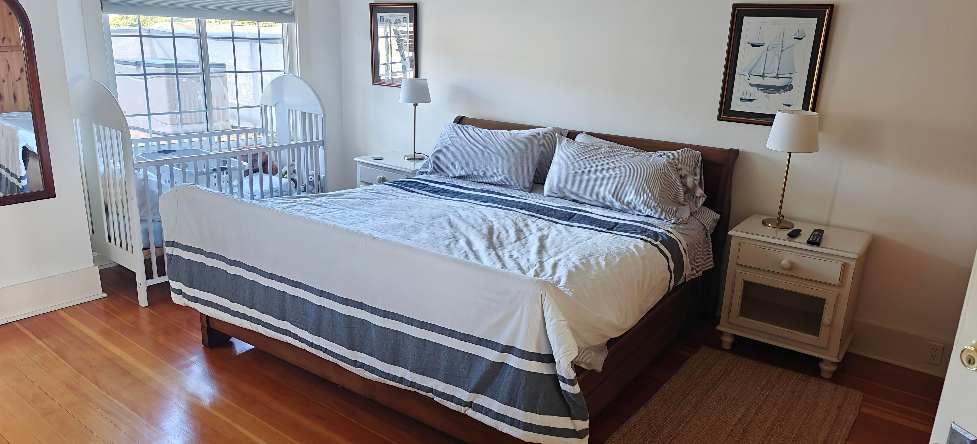 Un dormitorio con cama, mesita de noche, lámpara y una cuna.