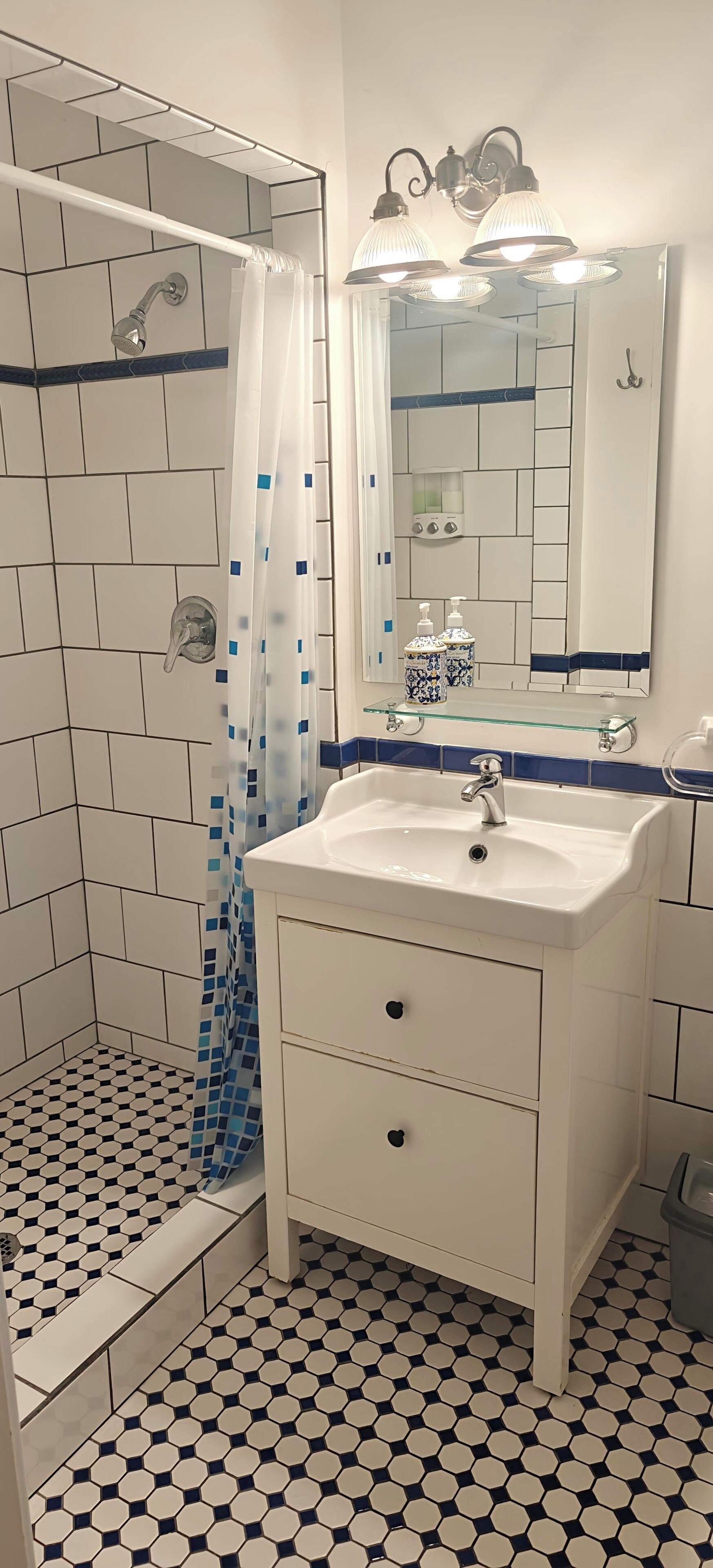 Une salle de bain avec une douche, un lavabo, un miroir et un sol carrelé.