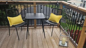 A wooden deck with a table and two chairs, a lantern, and a railing.