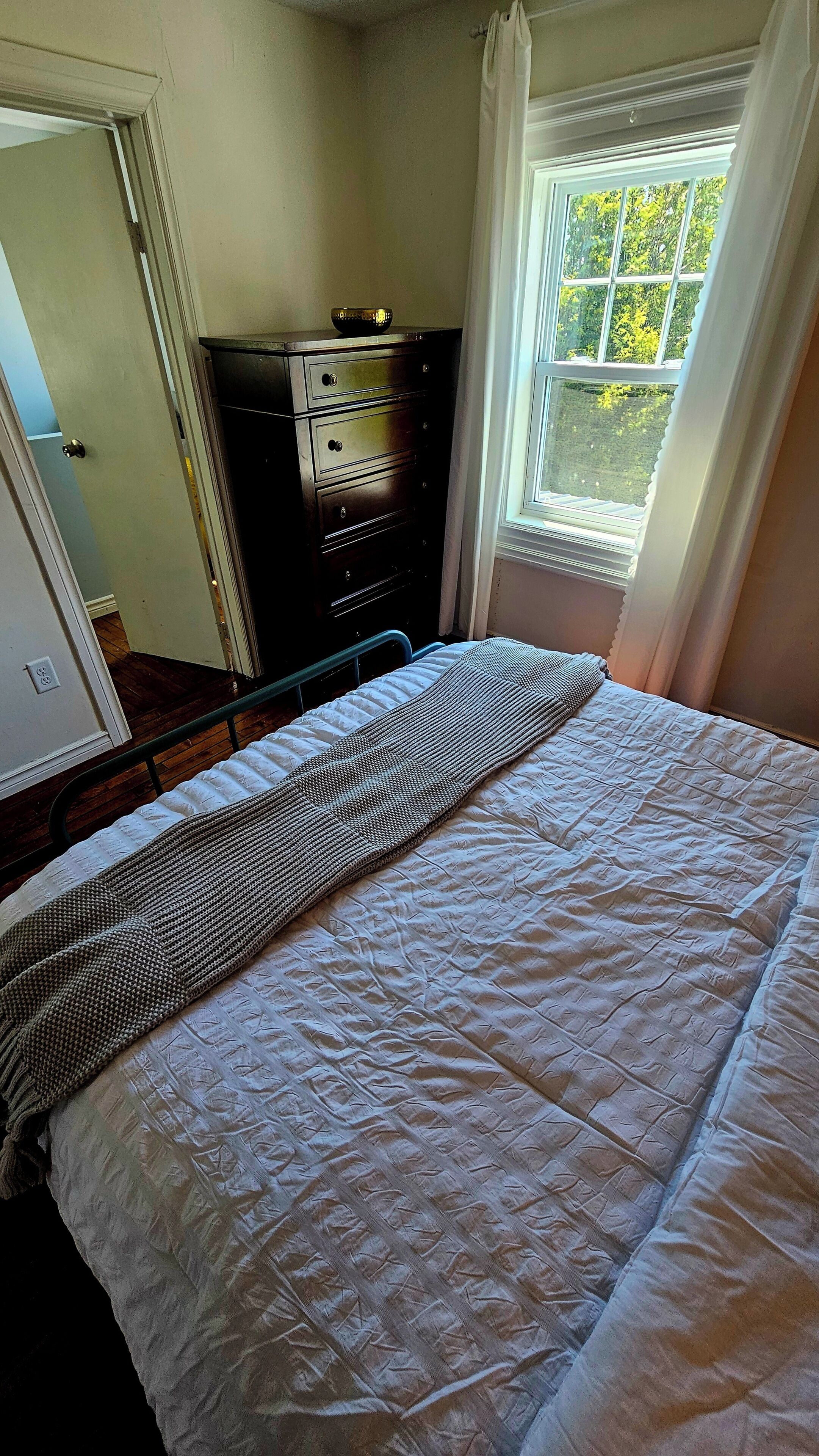 Een slaapkamer met een bed, een kapstok, een raam met gordijnen en een deur.