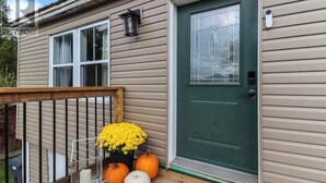 A house with a green door, a window with a decorative glass panel, and a wooden deck with pumpkins and flowers.