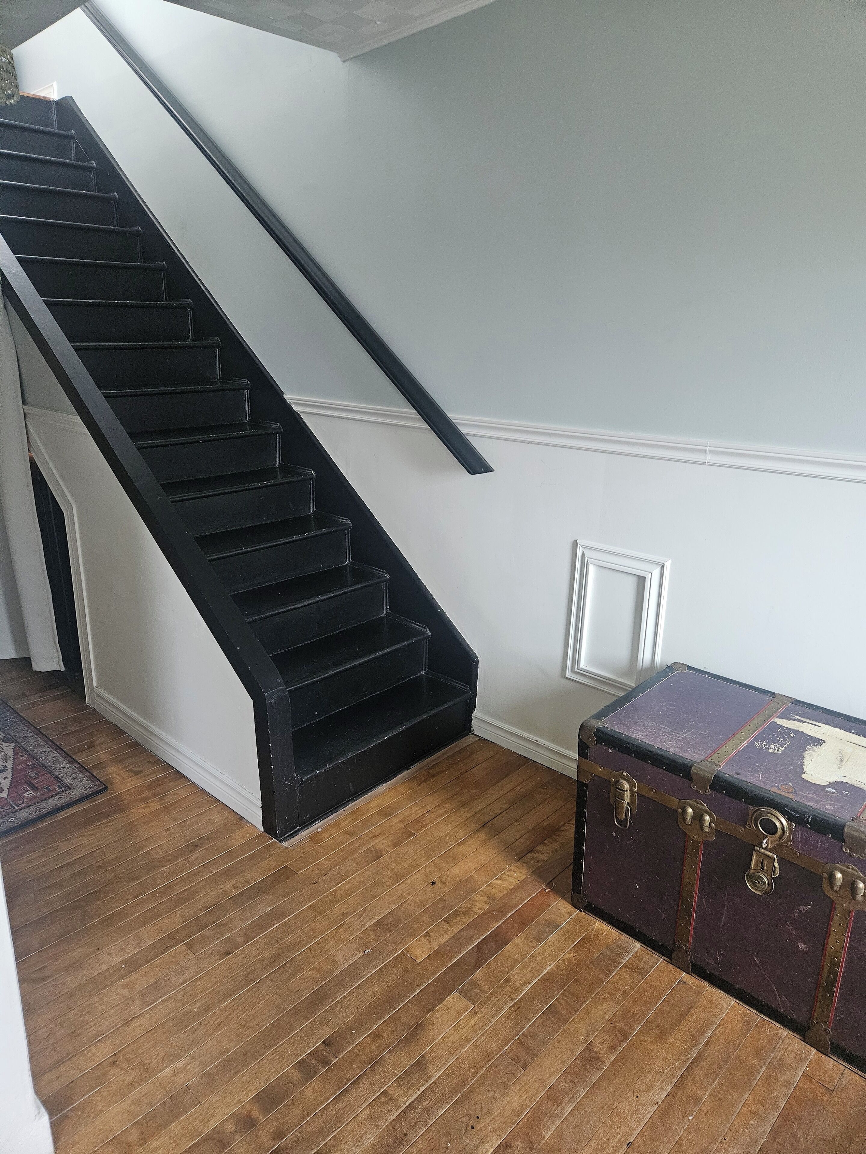 A staircase with black steps and white walls, a wooden floor, and a vintage suitcase.