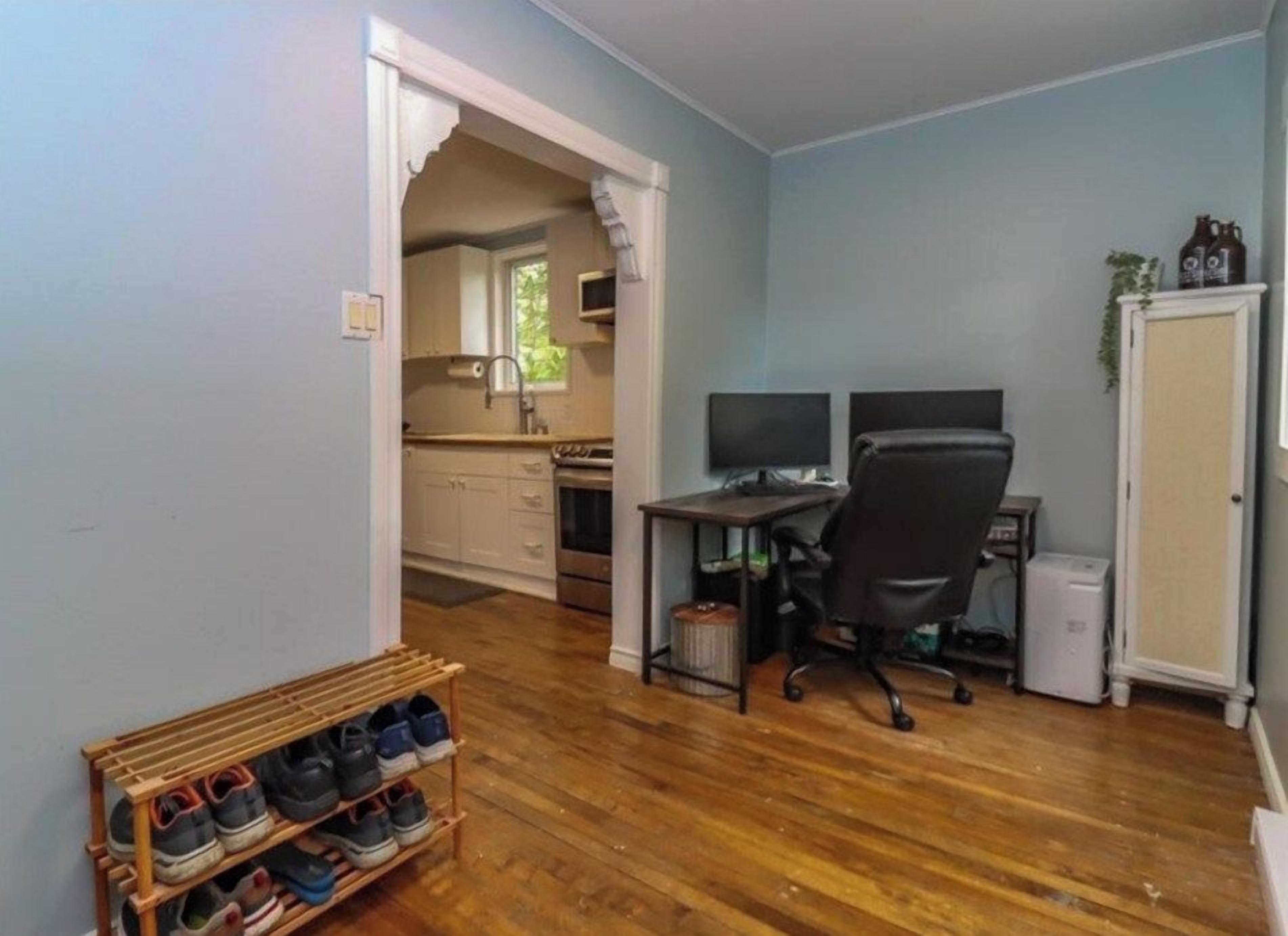 A room with a wooden floor, a desk with two monitors, a chair, a small cabinet, and a shoe rack.