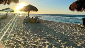Een strand met rieten parasols, een boot en de zon die boven de oceaan ondergaat.