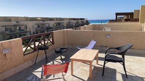 Een dakterras met een tafel en stoelen, met uitzicht op een kustgebied met gebouwen en een heldere lucht.