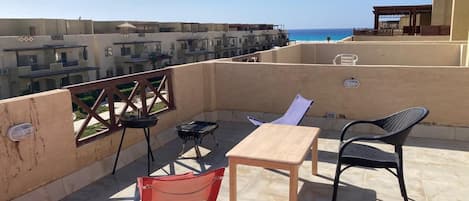 A rooftop terrace with a table and chairs, overlooking a coastal area with buildings and a clear sky.
