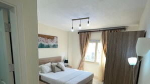 Een slaapkamer met een bed, nachtkastje, lamp en een schilderij aan de muur.