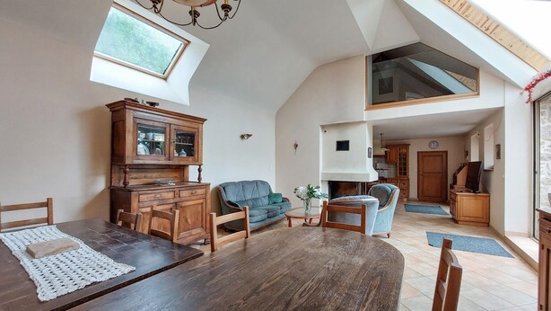Un vaste salon doté d’un haut plafond, avec une table à manger, un canapé et un coin cuisine visible à travers une porte ouverte.