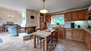 Une cuisine spacieuse dotée de meubles en bois, d’un îlot central et d’une cheminée. On y trouve également un coin repas avec une table et des chaises.