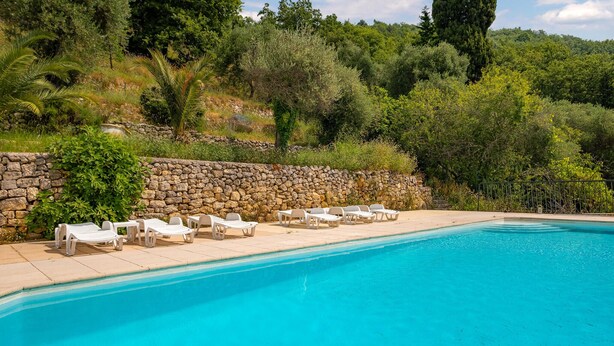 A swimming pool with white lounge chairs and a stone wall. - Charmante villa vue mer (Grasse Magagnosc)