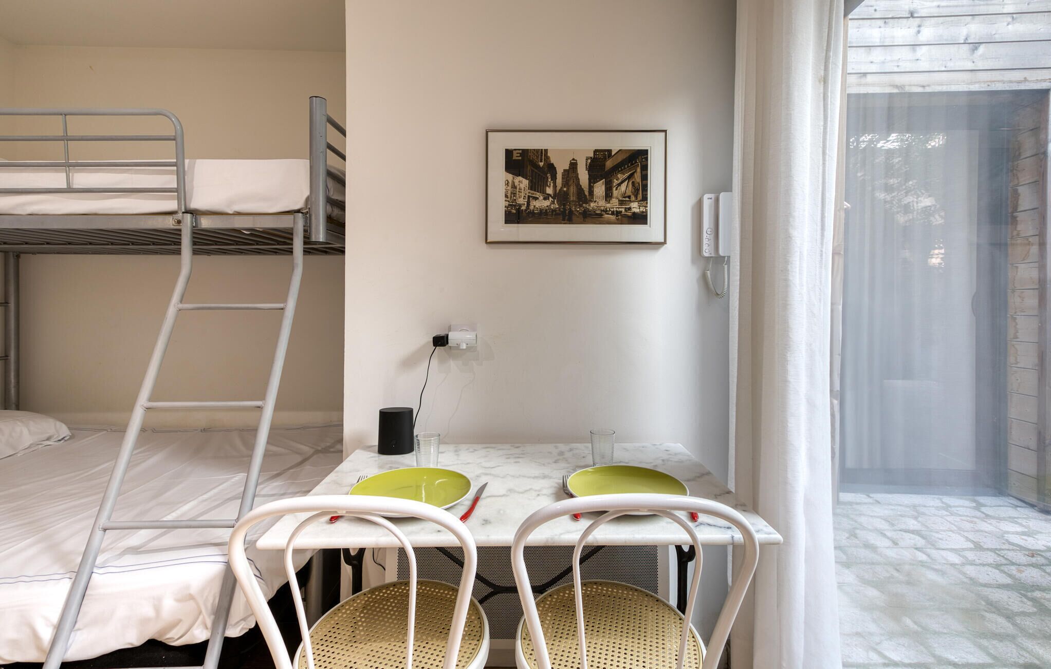 A bunk bed room with a table and chairs, a picture on the wall, and a phone.
