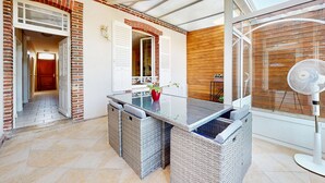 Eine sonnendurchflutete Terrasse mit einem Glastisch, Korbmöbeln und einem Ventilator.