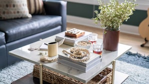 A living room with a sofa, a coffee table with books, a vase with flowers, and a guitar in the background. - Sleeps 36, 3 Homes Walk to Germantown Modern Townhomes Near DT Avantstay (Nashville)