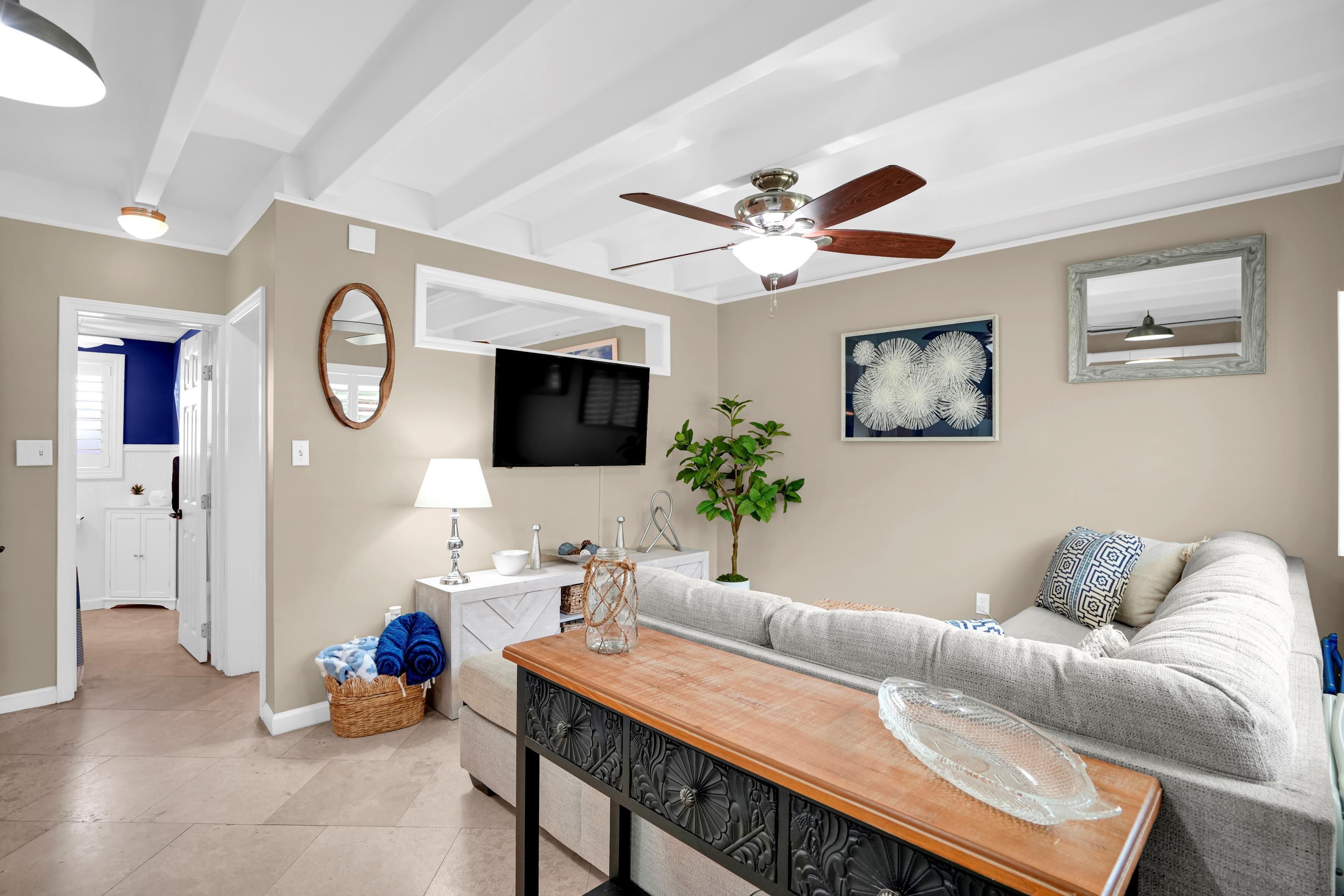 Un soggiorno moderno con una ventola a soffitto, una TV a schermo piatto, un tavolino in legno, un divano grigio e un'area da pranzo.