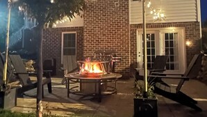 Un espace patio avec un foyer, des sièges d’extérieur et des guirlandes lumineuses.