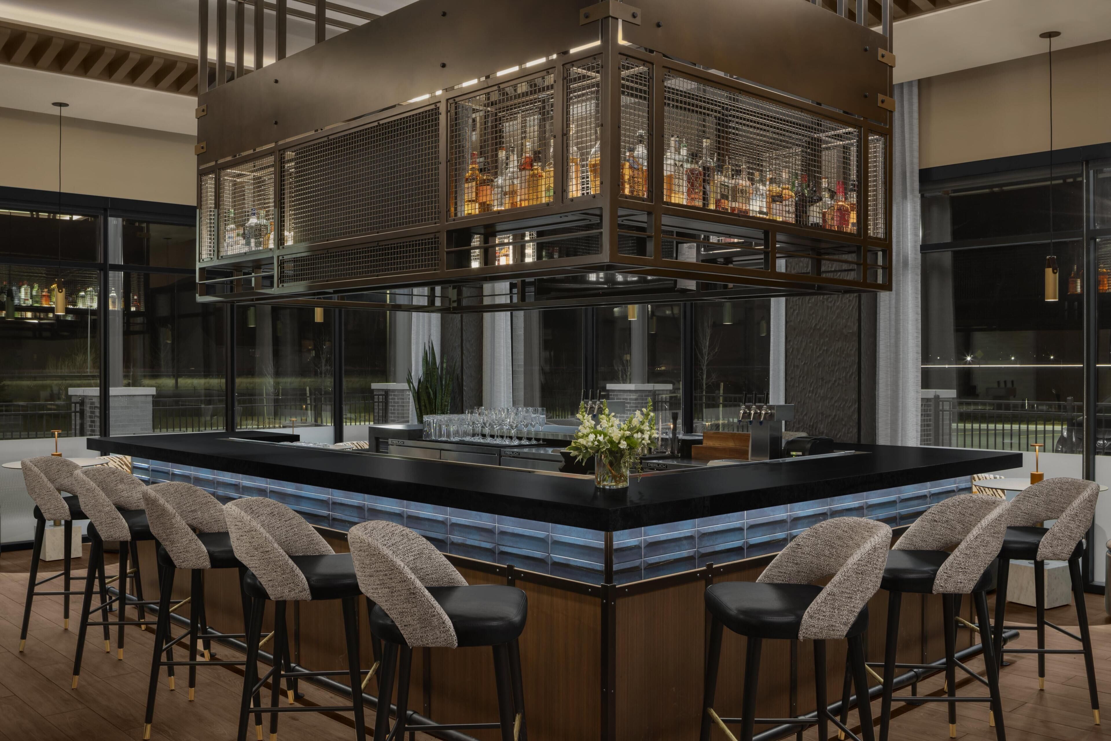 Un área de bar con una barra alta, varios taburetes y un ventanal grande.