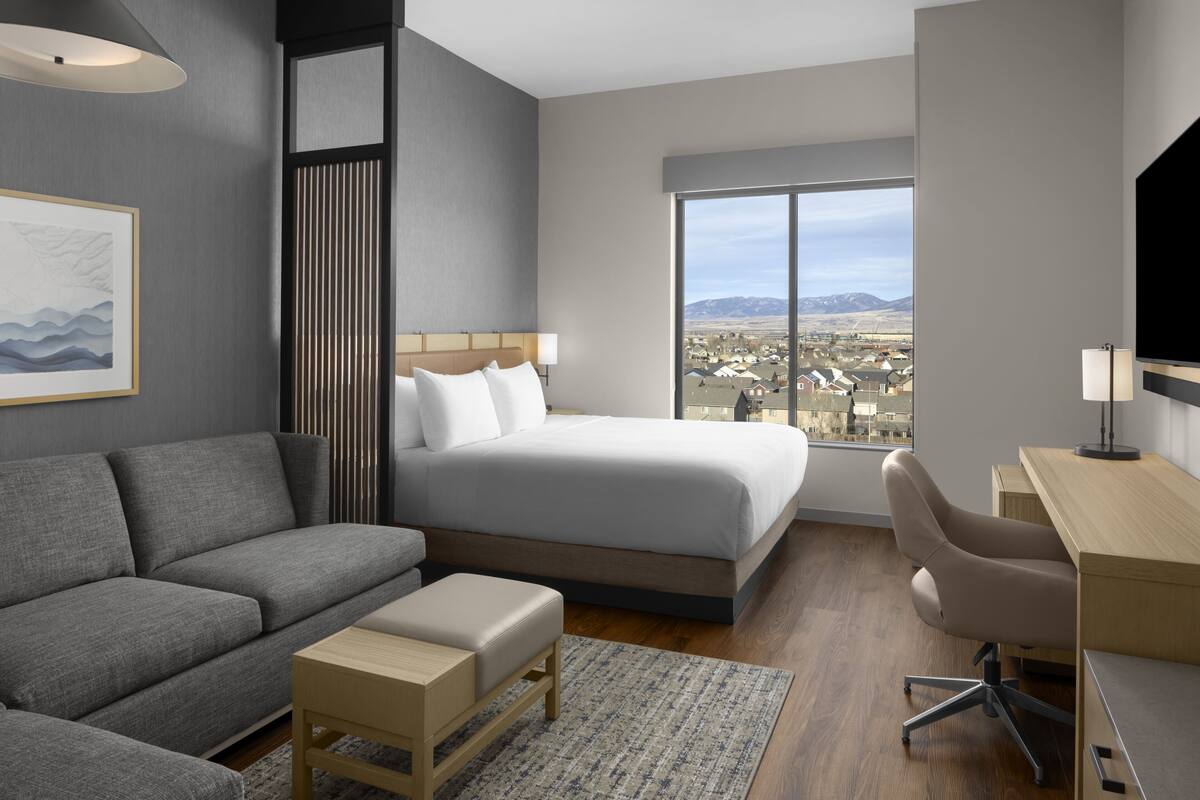 Una habitación de hotel moderna con cama, sofá, escritorio y un amplio ventanal con vistas a la ciudad.