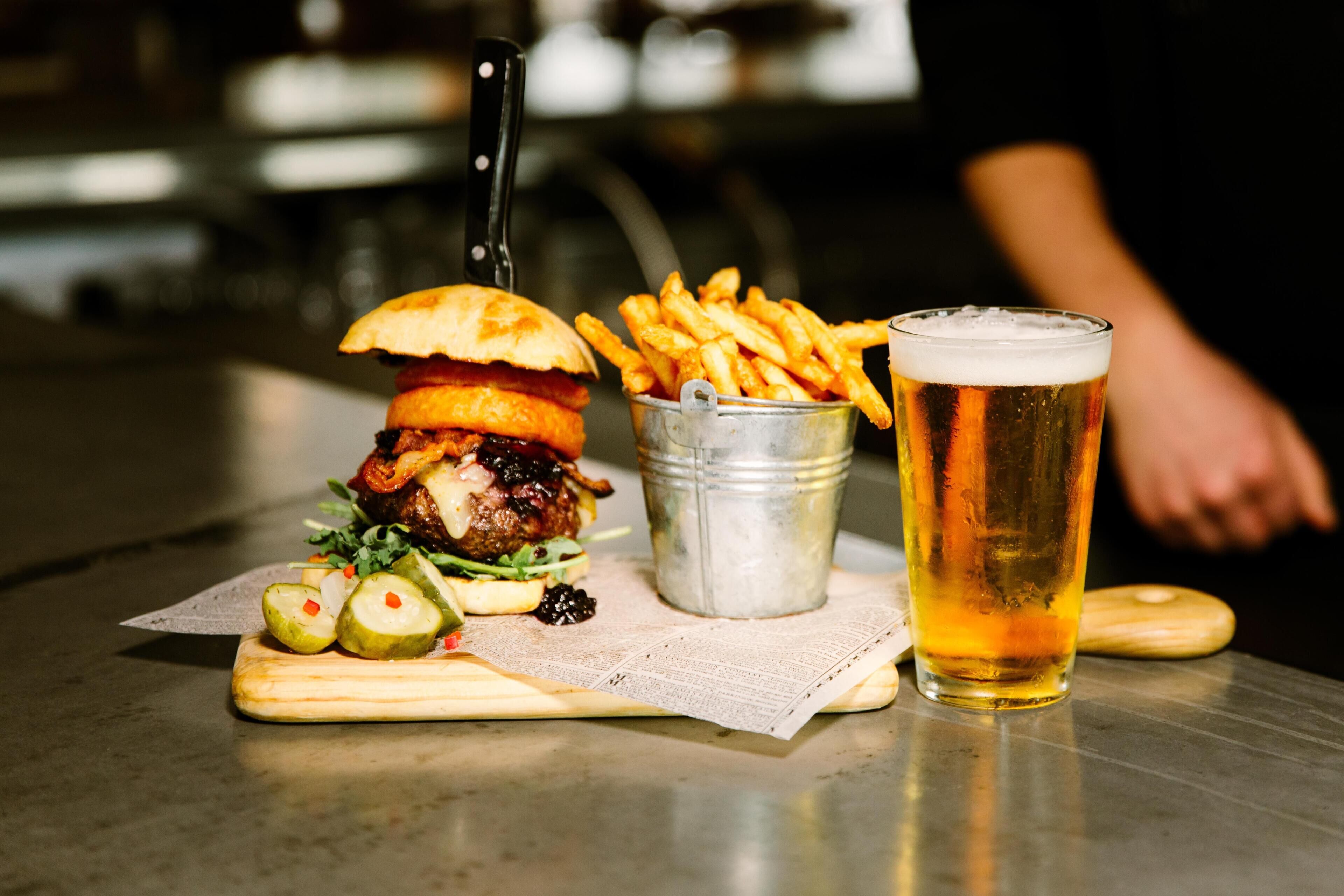 A meal consisting of a burger, fries, and a beer on a table.