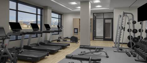 A gym with treadmills, weight machines, and a view of mountains through large windows.