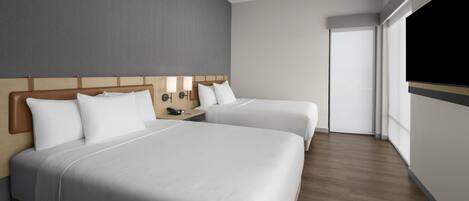 Una habitación de hotel con dos camas, un cabecero de madera, una mesita de noche con lámpara y un ventanal grande.