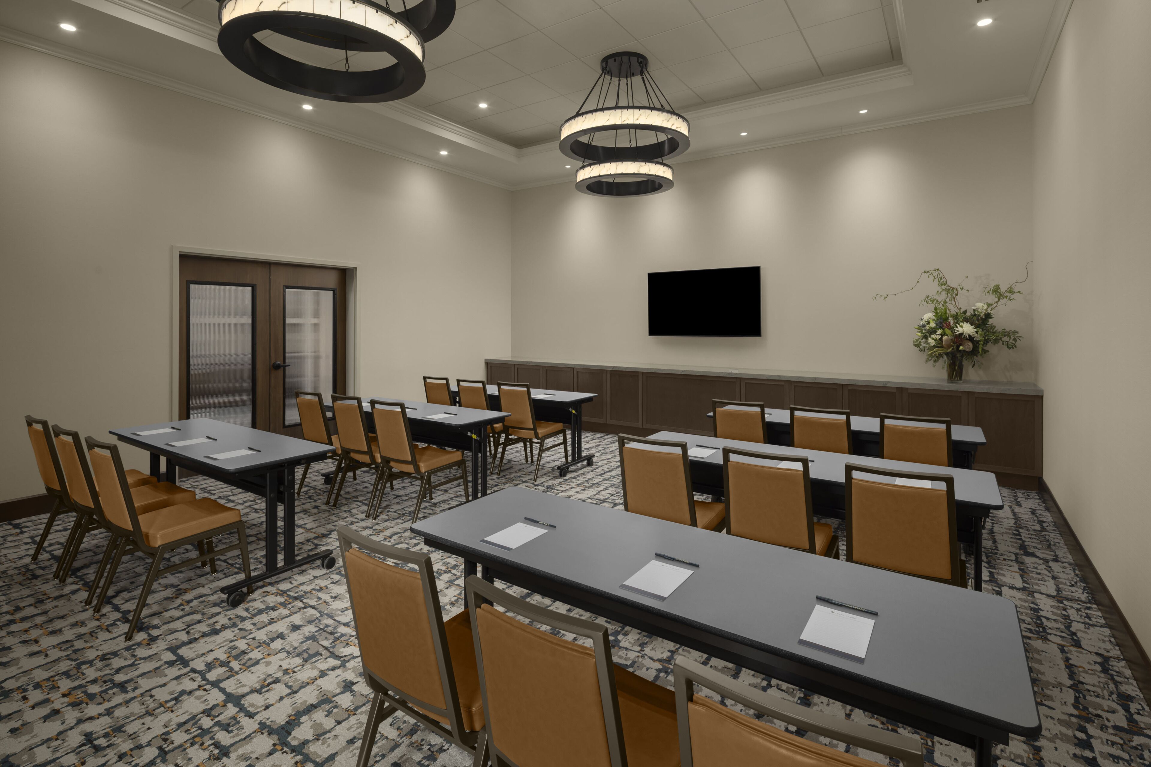 Une salle de conférence équipée de tables, de chaises, d’un téléviseur à écran plat et d’une porte.