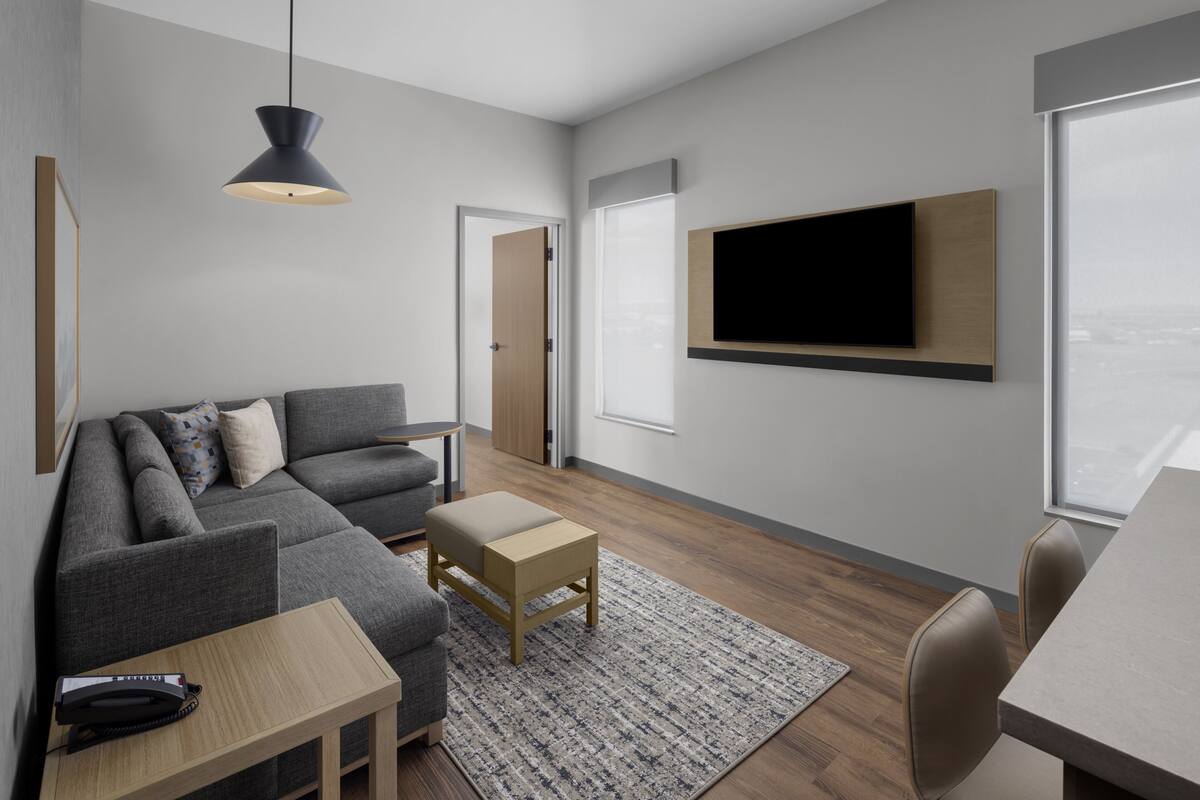Una sala de estar moderna con un sofá, una mesita, un televisor montado en la pared y vistas de la ciudad a través del ventanal.