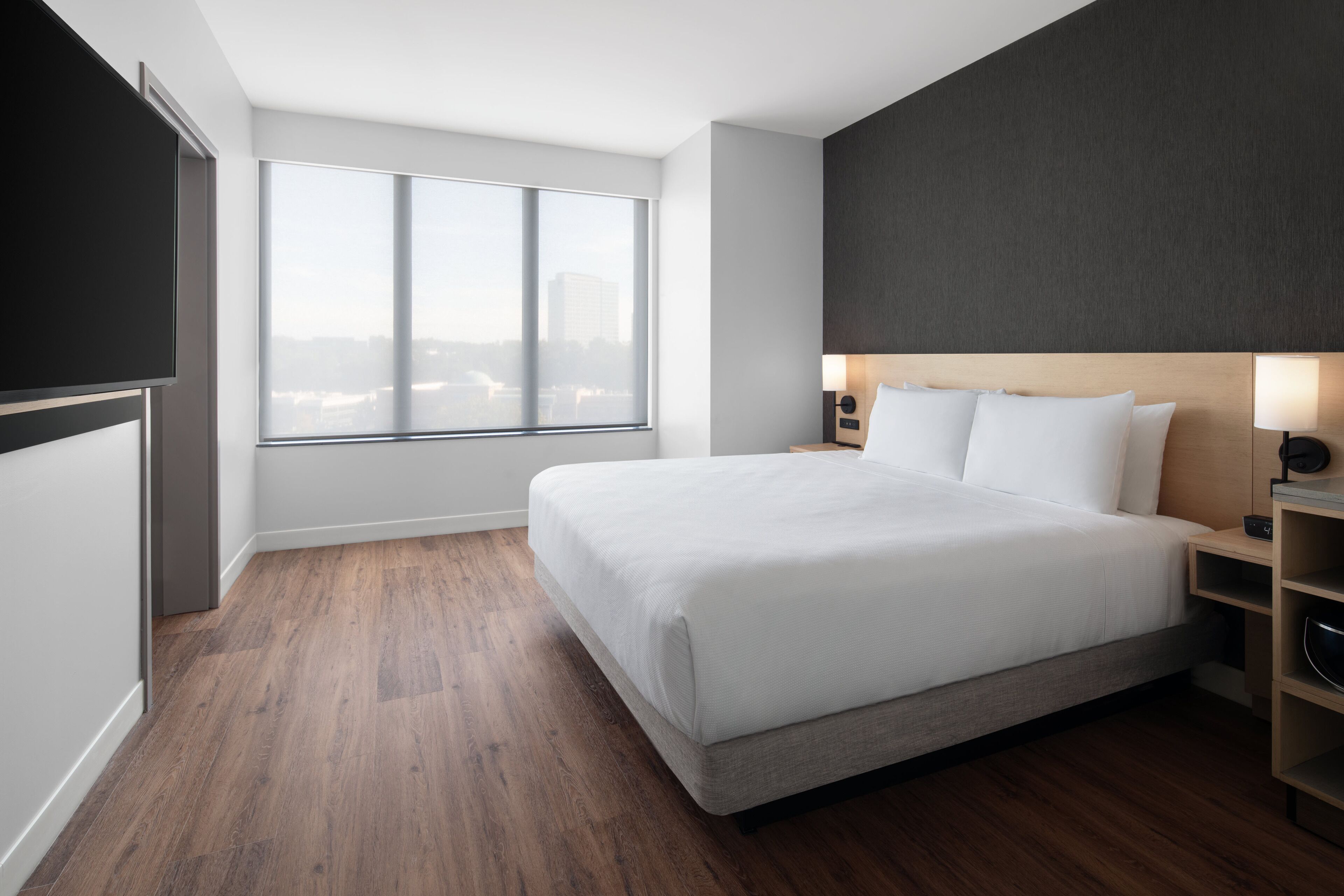 Une chambre d’hôtel moderne dotée d’un grand lit, d’une vue sur la ville, d’un téléviseur à écran plat et d’un plancher en bois.