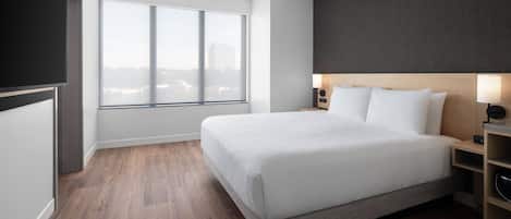 Une chambre d’hôtel moderne dotée d’un grand lit, d’une vue sur la ville, d’un téléviseur à écran plat et d’un plancher en bois.