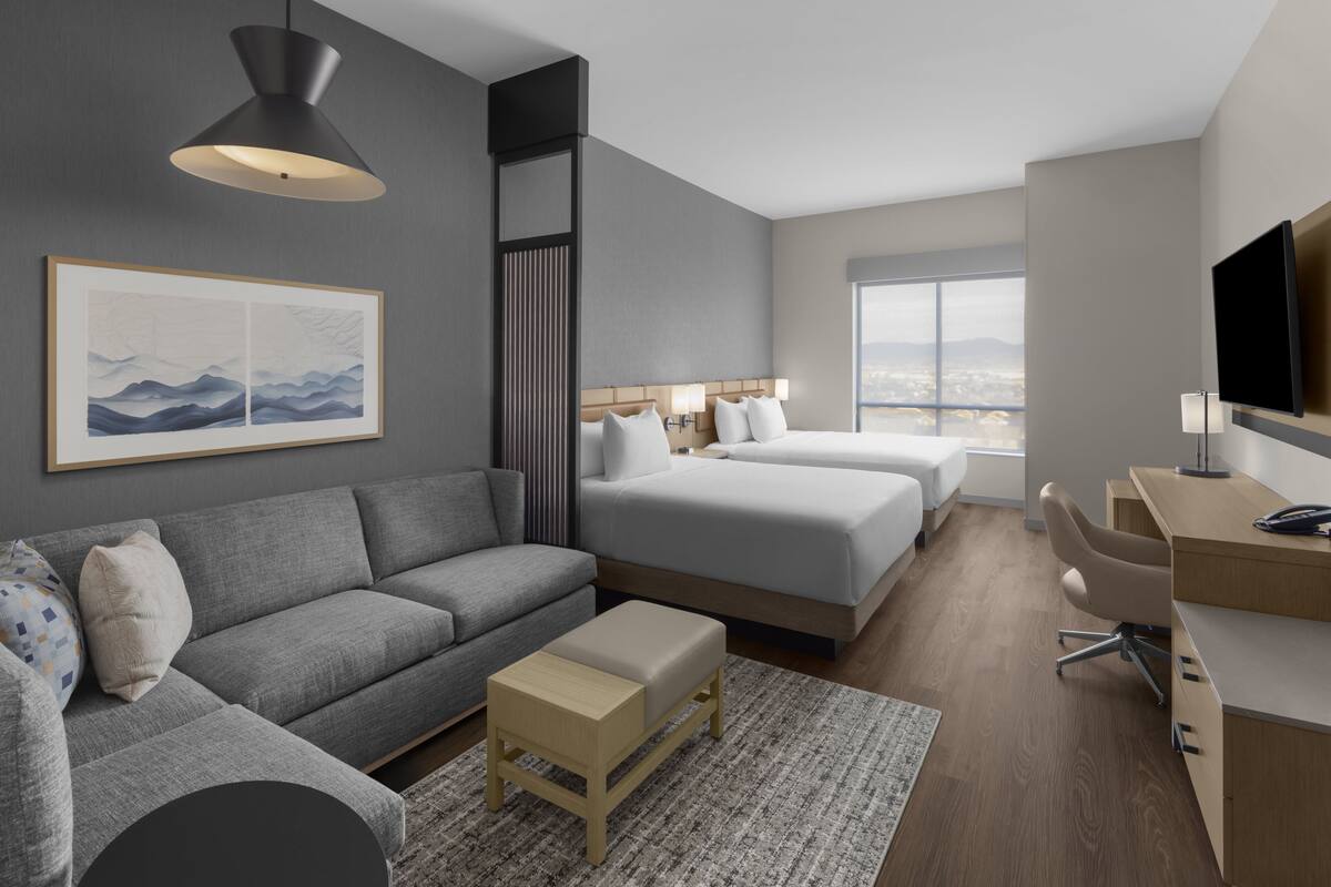 Habitación de hotel moderna con un sofá gris, dos camas, un escritorio y un televisor.