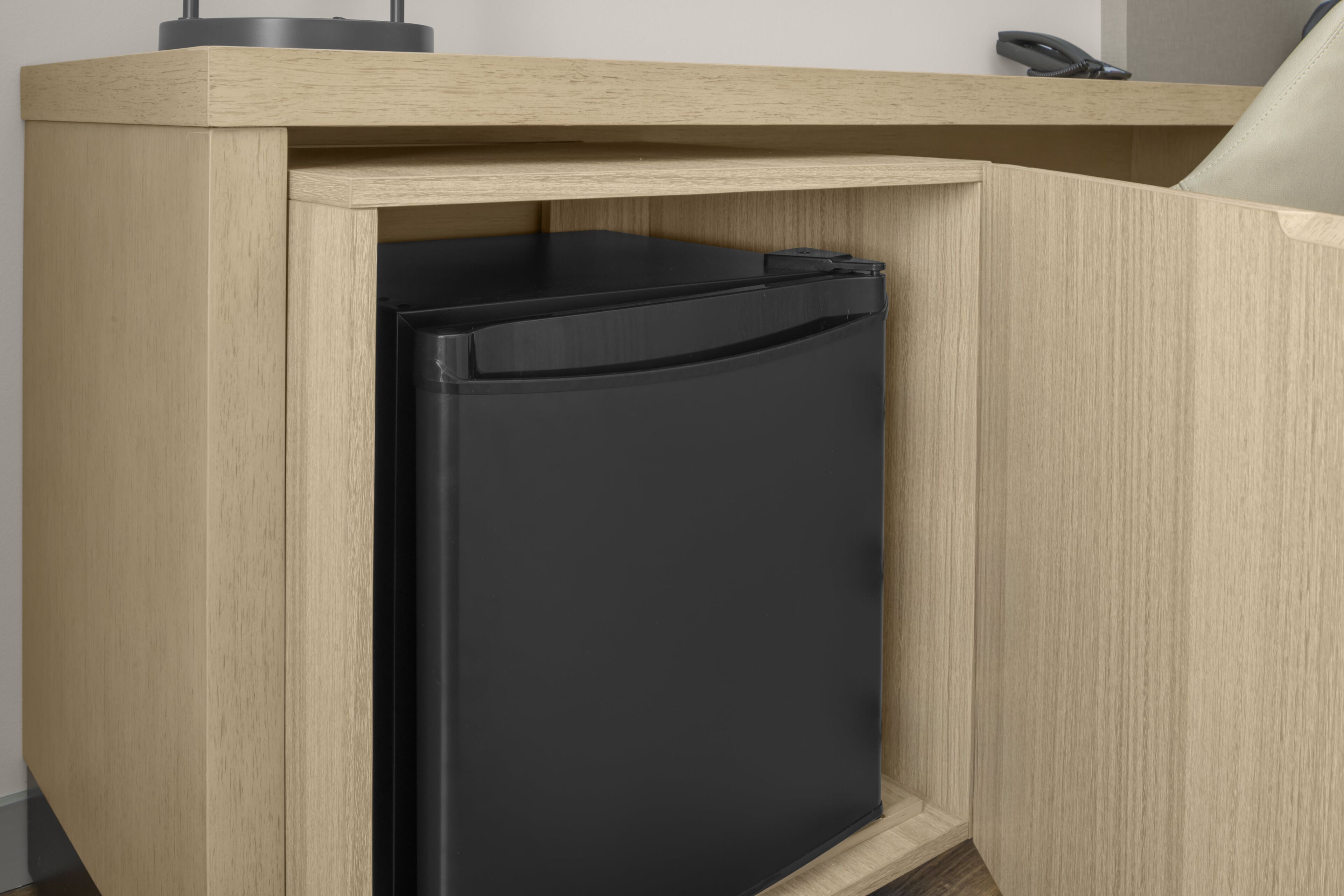 A compact, built-in black refrigerator in a wooden cabinet with a light wood finish.