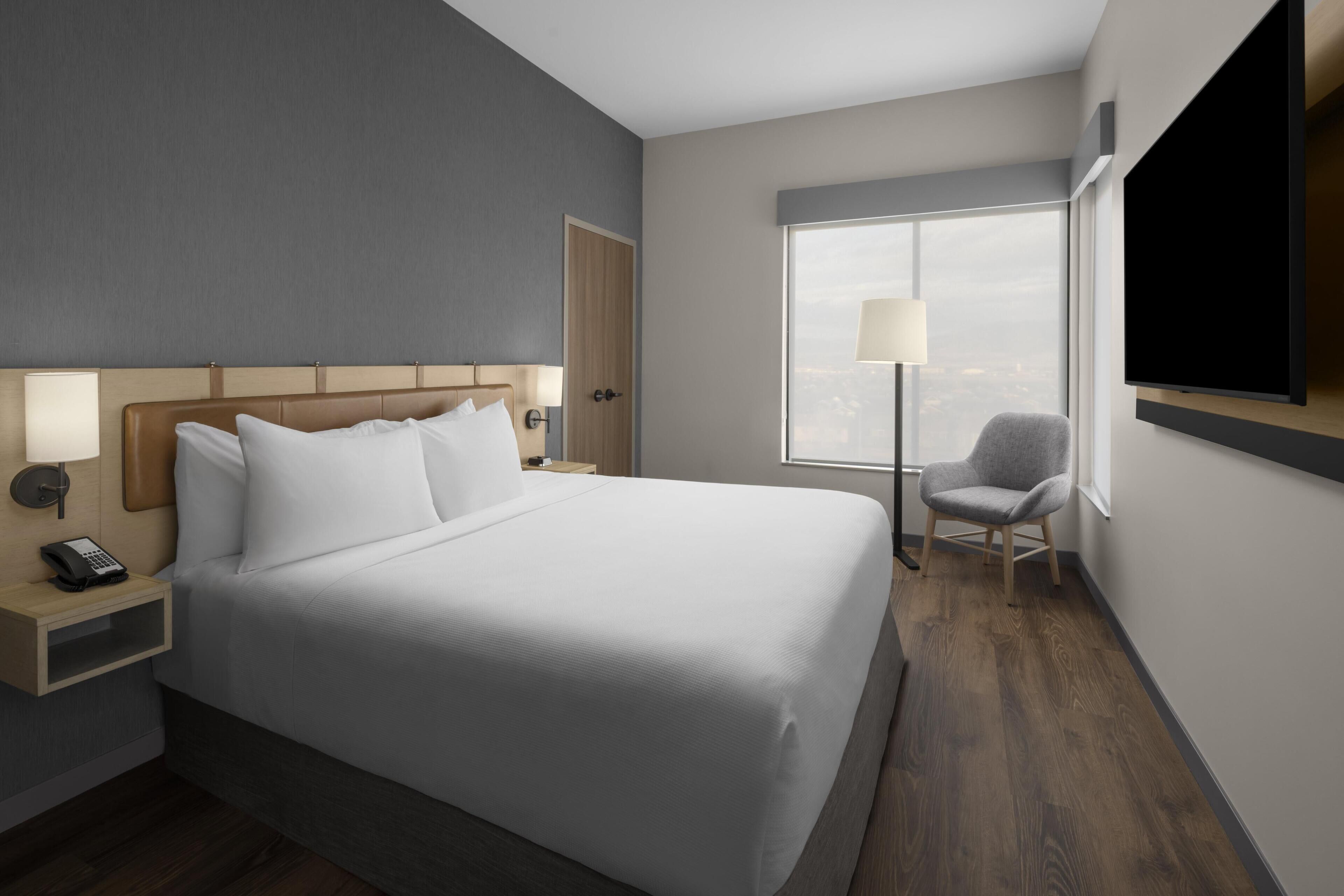 A hotel room with a large bed, bedside lamps, a desk with a phone, a chair, a TV, and a window with a view.